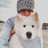 Personne portant un bonnet gris tenant un chien blanc à pelage épais.