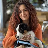 Jeune femme aux cheveux bouclés et longs tenant un chiot noir et blanc dans ses bras, souriant doucement.