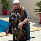 Homme assis au bord d'une piscine avec un grand chien noir et gris à ses côtés.