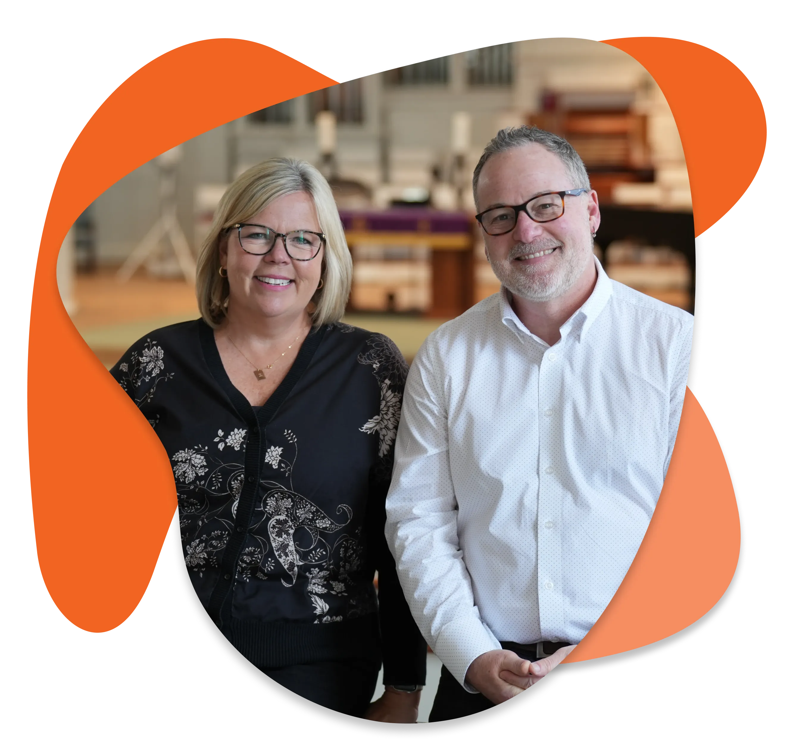 Smiling man and woman wearing glasses seated in a softly lit room with blurred background.