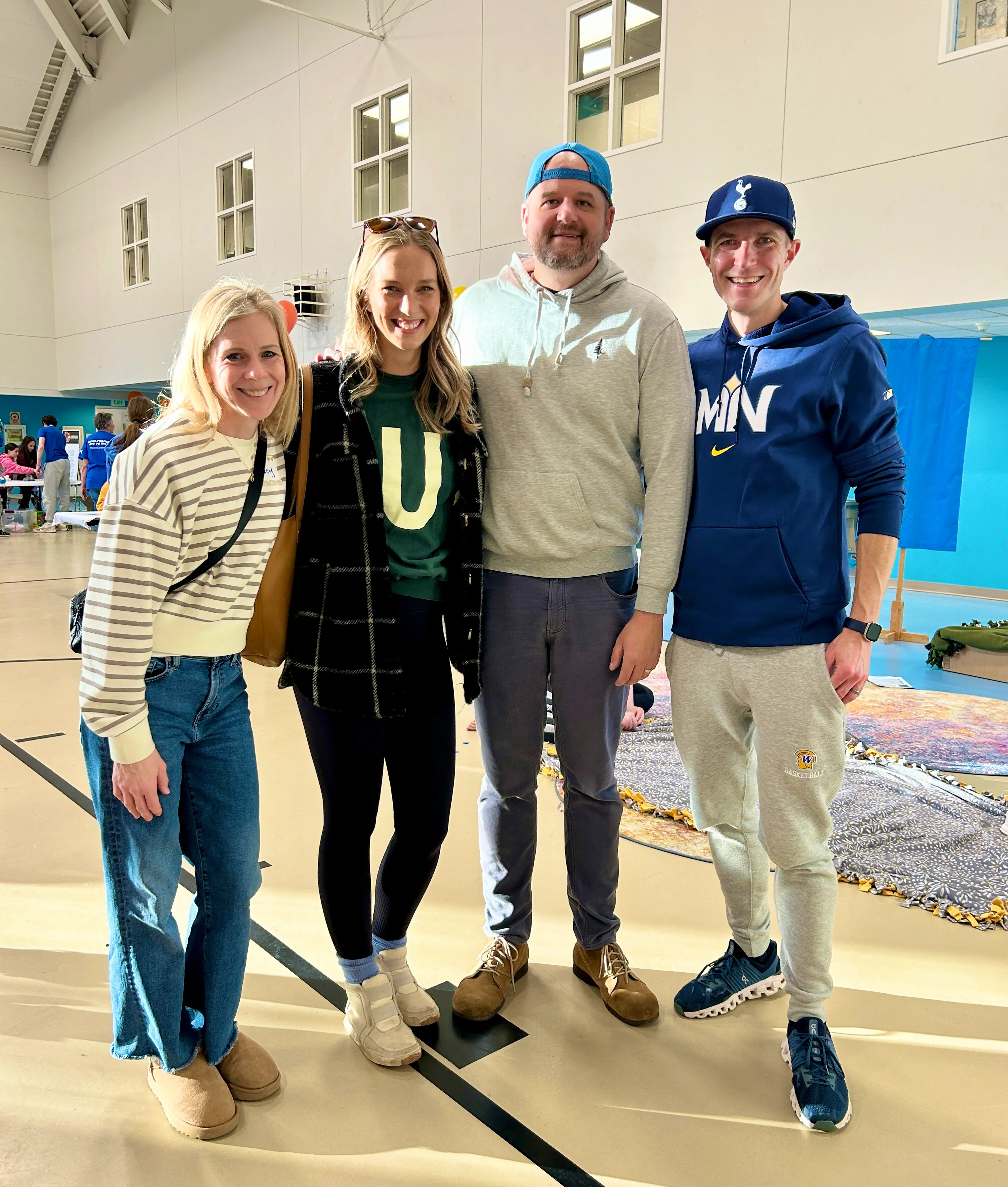 Four adults standing together indoors, smiling at the camera, with two women on the left and two men on the right.