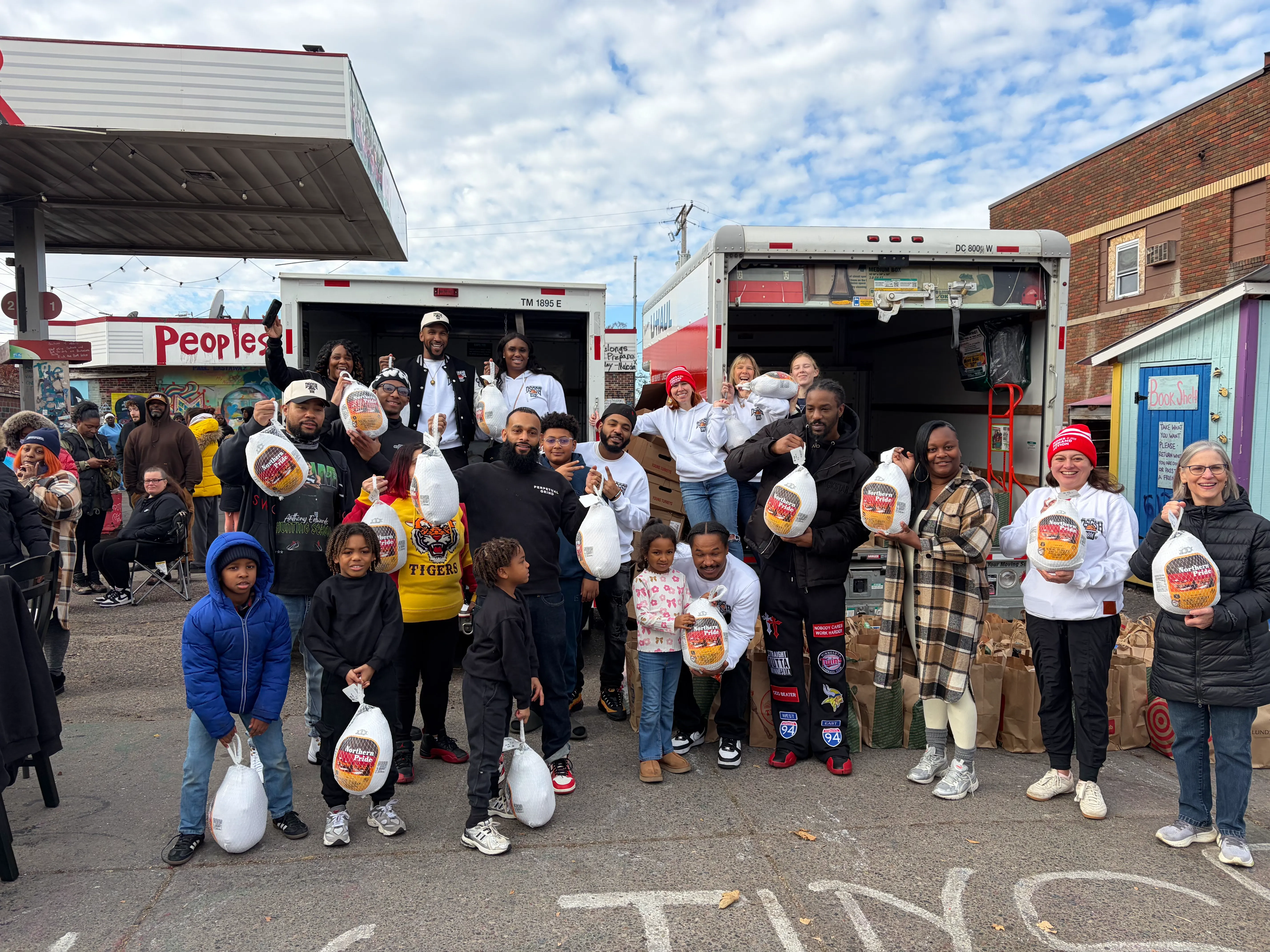 Group of people, including children, holding frozen turkeys in front of two trucks during a community turkey giveaway event.
