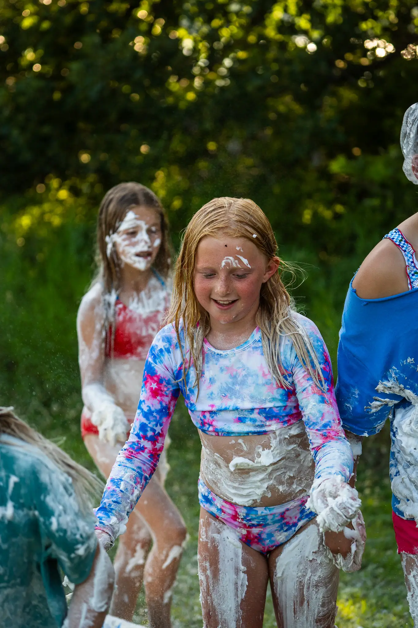 Children playing outdoors covered in white foam or shaving cream, smiling and having fun.