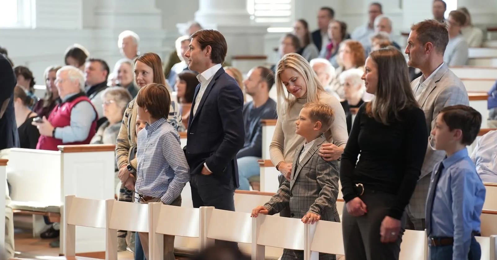 Families and children dressed formally standing in a church during a confirmation ceremony with a seated congregation in the background.