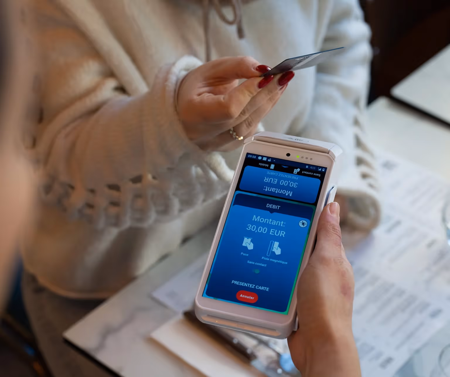 Personne tenant une carte bancaire près d'un terminal de paiement affichant un montant de 30,00 EUR.