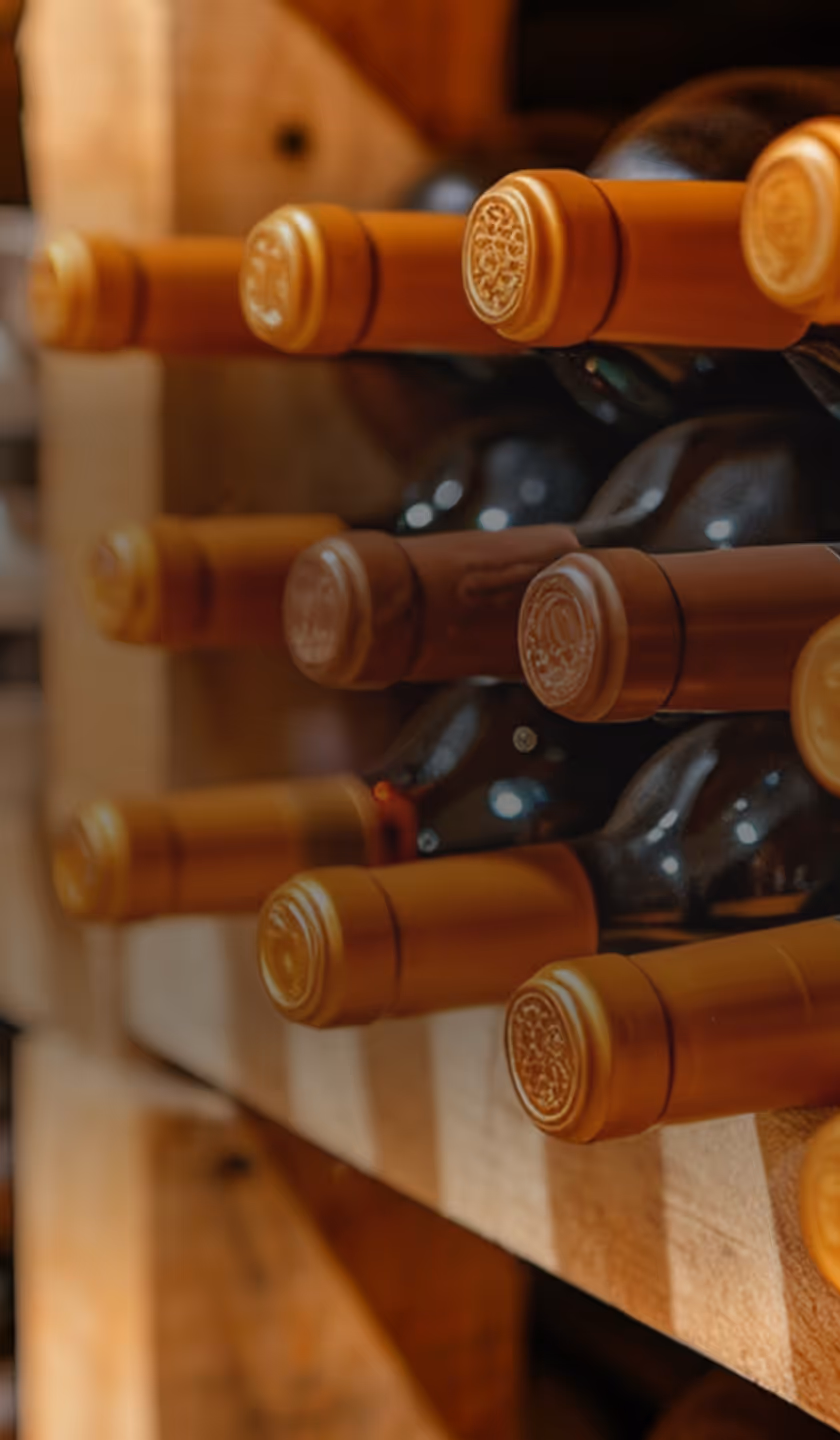 Rangée de bouteilles de vin avec capsules dorées, stockées horizontalement dans une cave en bois.
