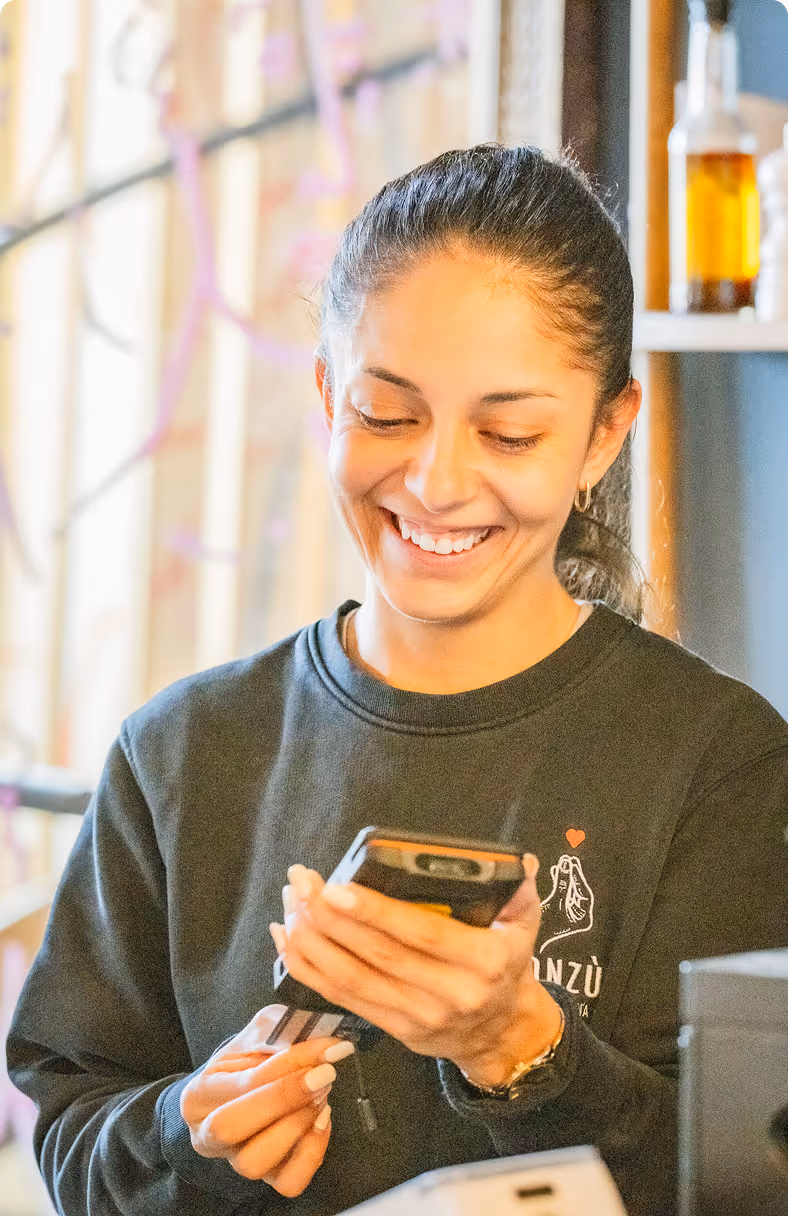 Jeune femme souriante utilisant un terminal de paiement mobile avec une carte bancaire dans un environnement lumineux.