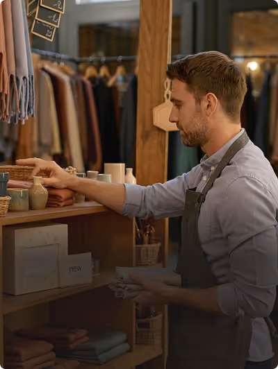 Homme en tablier arrangeant des articles décoratifs sur une étagère dans un magasin.