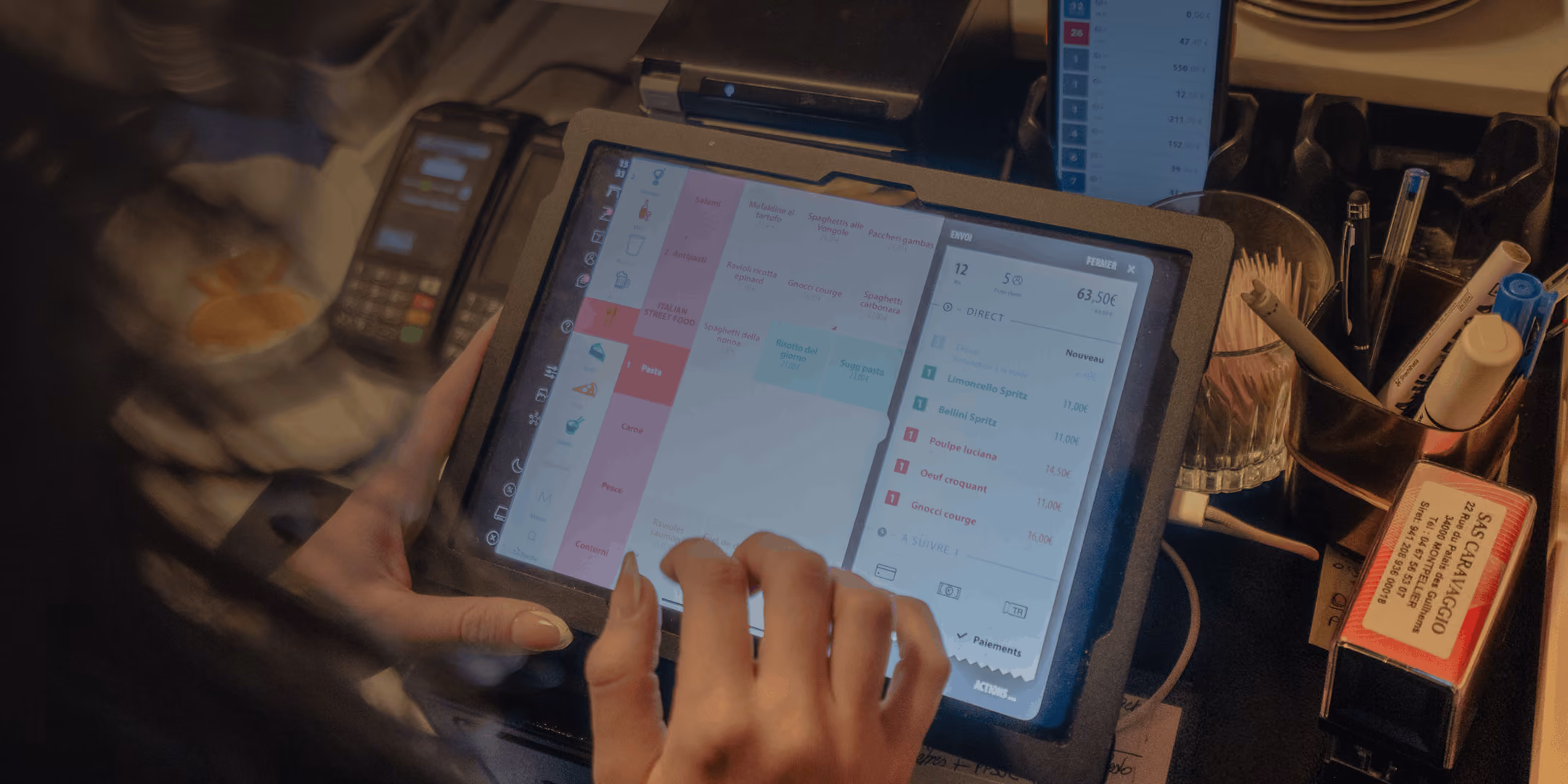 Main d'une personne utilisant une caisse enregistreuse tactile à Montpellier avec menu et commande affichés.