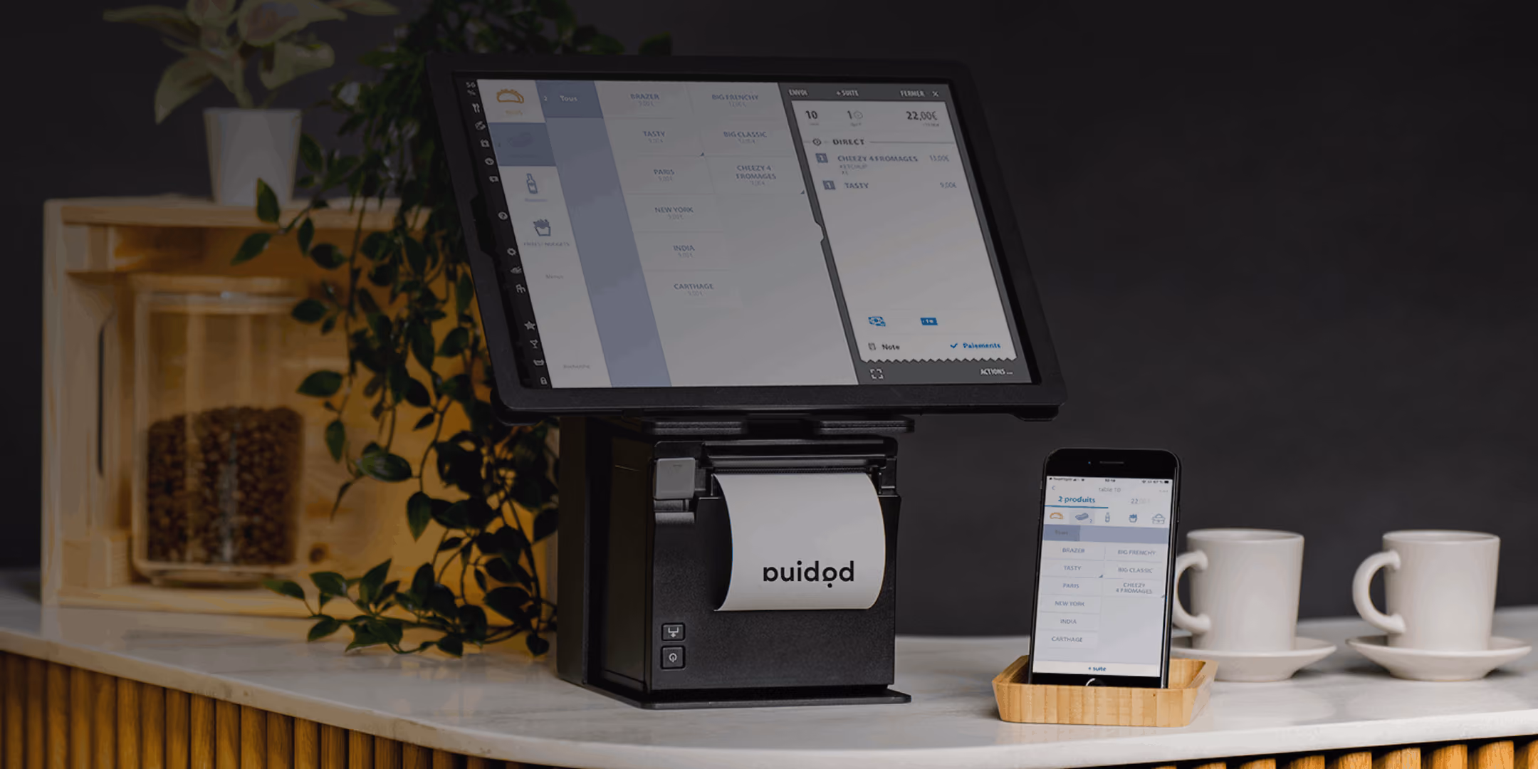 Caise enregistreuse tactile à Agen avec reçu, smartphone affichant une commande, et deux tasses sur un comptoir.