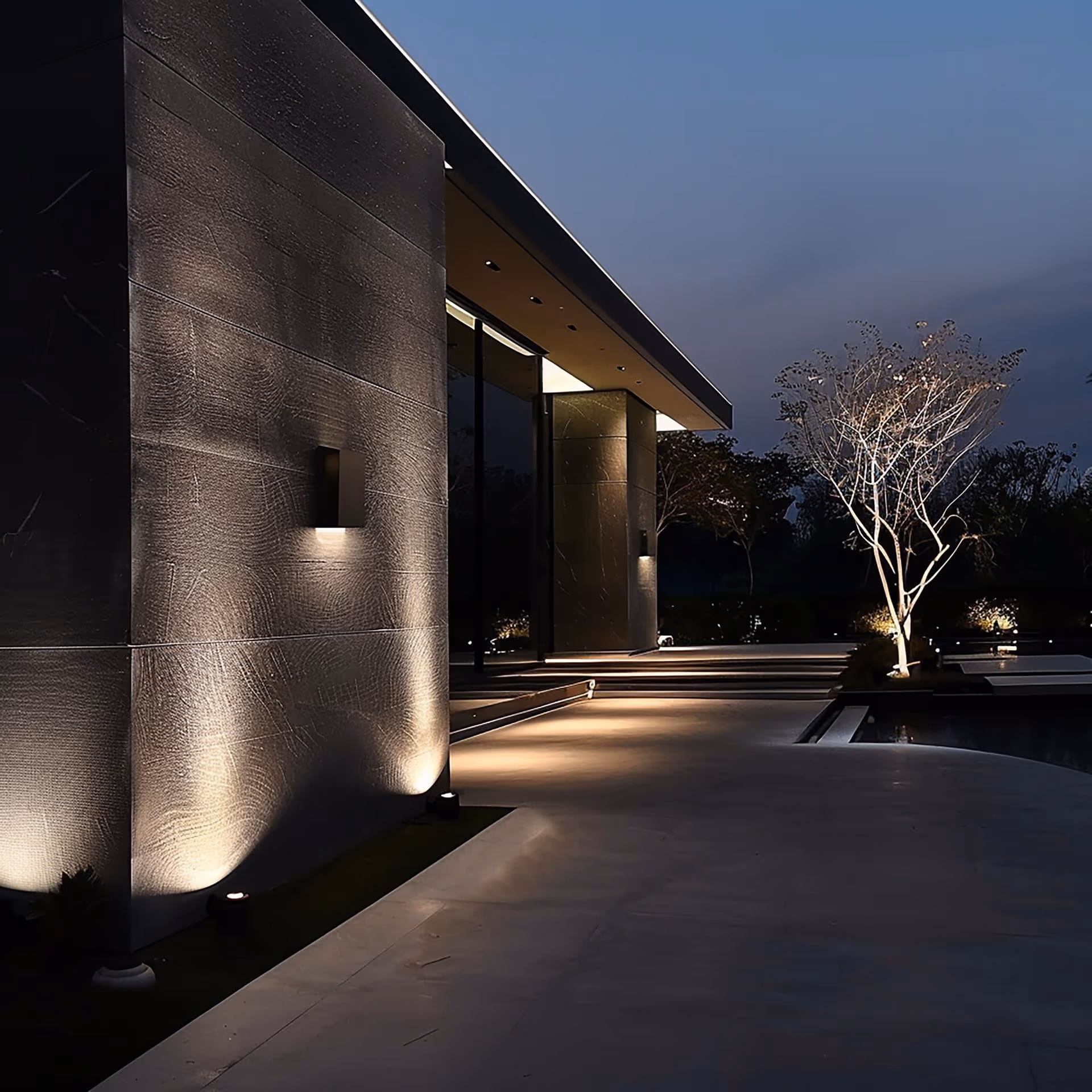 Modern building exterior at night with illuminated walls, a lit tree, and minimal outdoor lighting.