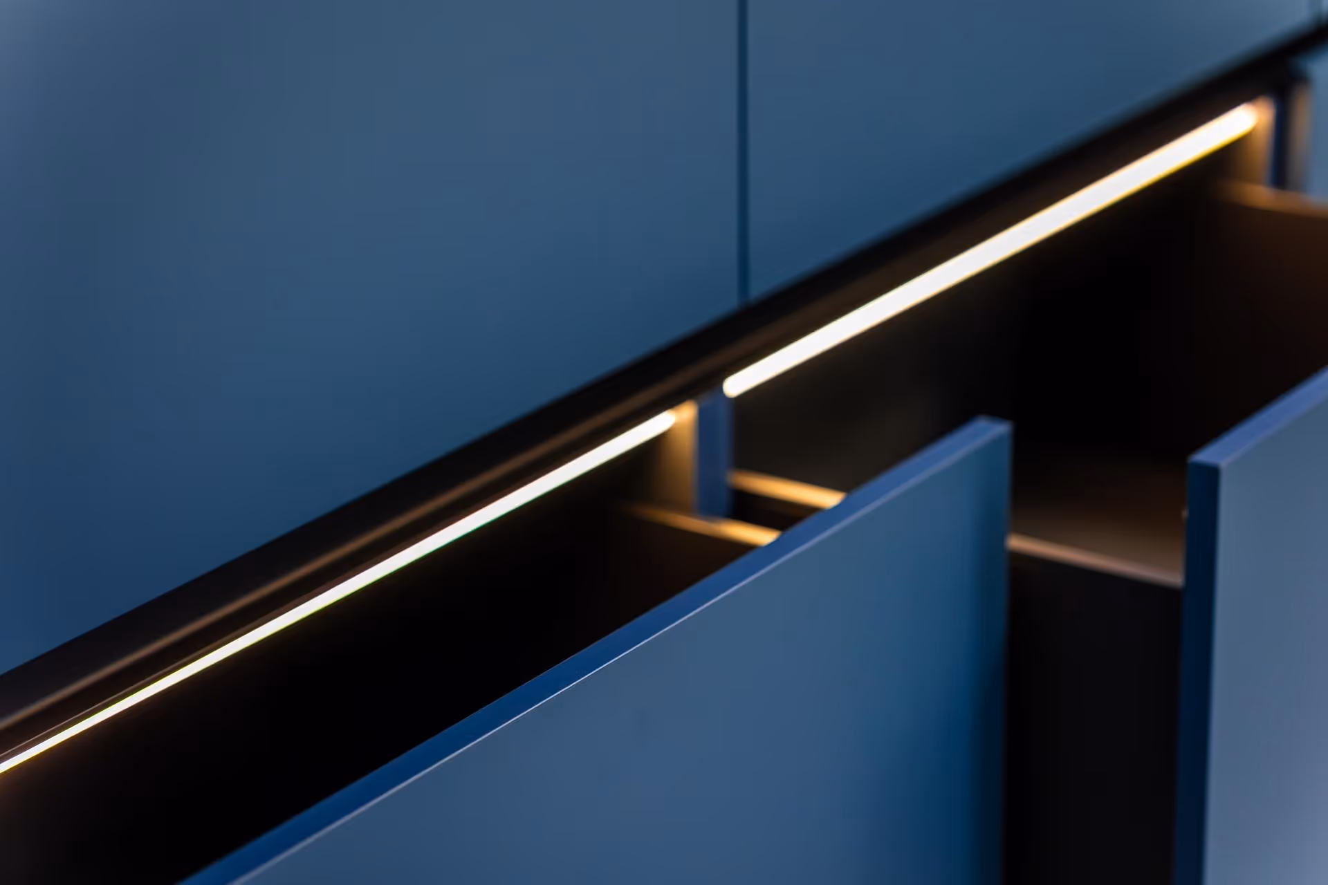 Close-up of modern blue cabinet drawers with built-in warm LED lighting.