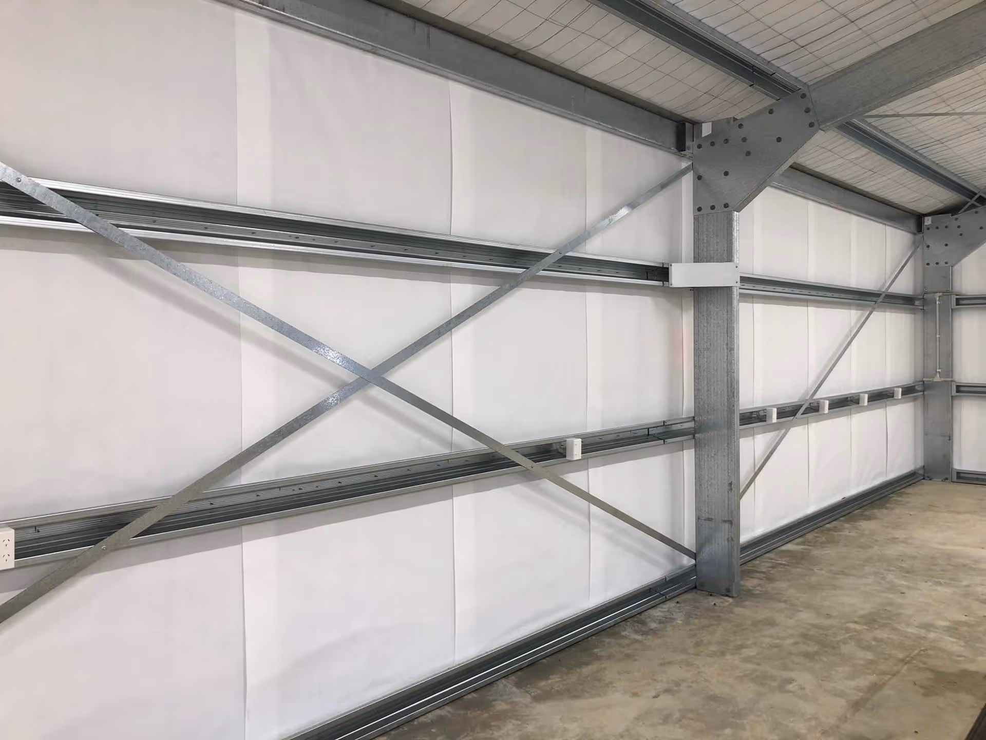 Interior of a large industrial warehouse with steel beams and cross-bracing against white insulated walls, conveying a sense of structural strength.