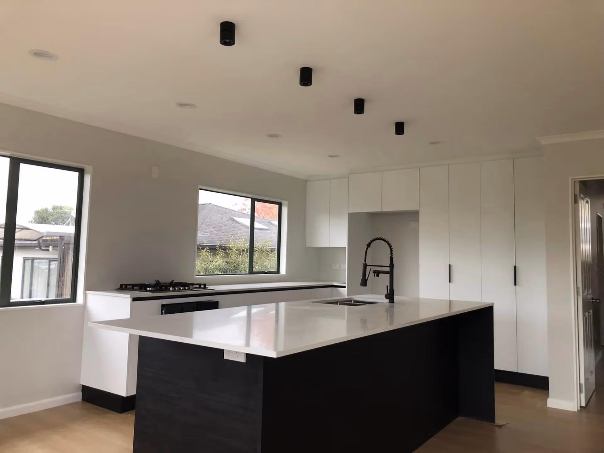 Modern kitchen with black and white color scheme featuring a large island with a white countertop, black faucet, sleek cabinets, and minimalist lighting.