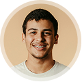 Smiling young man with short dark hair wearing a light-colored shirt against a beige background.
