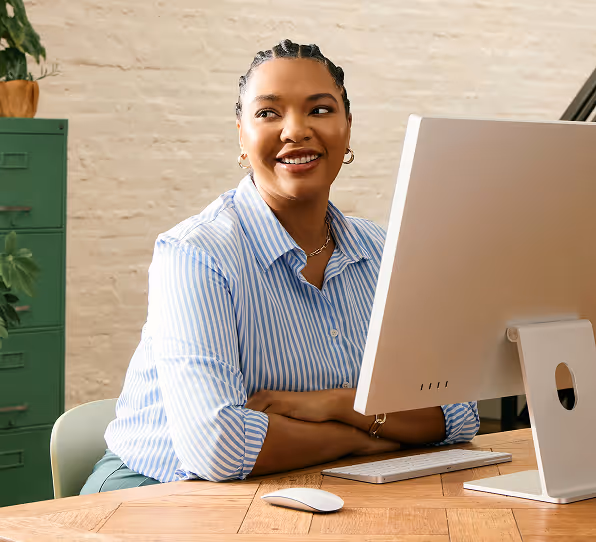 Smiling woman in striped shirt sitting at a desk using a desktop computer.