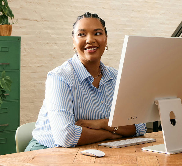 Smiling woman in striped shirt sitting at a desk using a desktop computer.