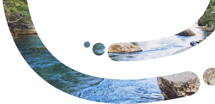 Curved composition photo of a flowing river with rocks and green trees on the riverbanks.