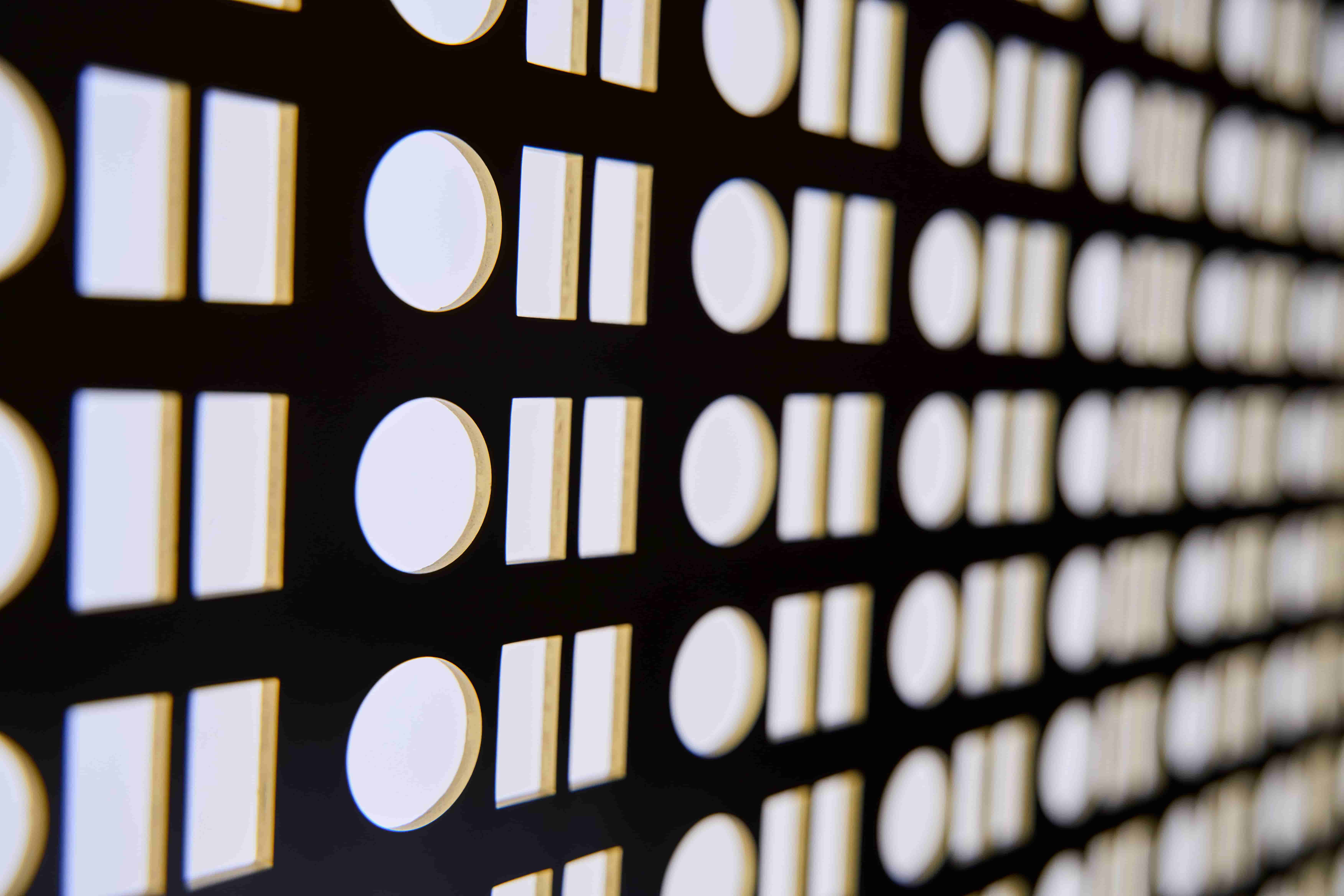 Close-up of a black panel with alternating circular and rectangular white illuminated buttons arranged in rows.