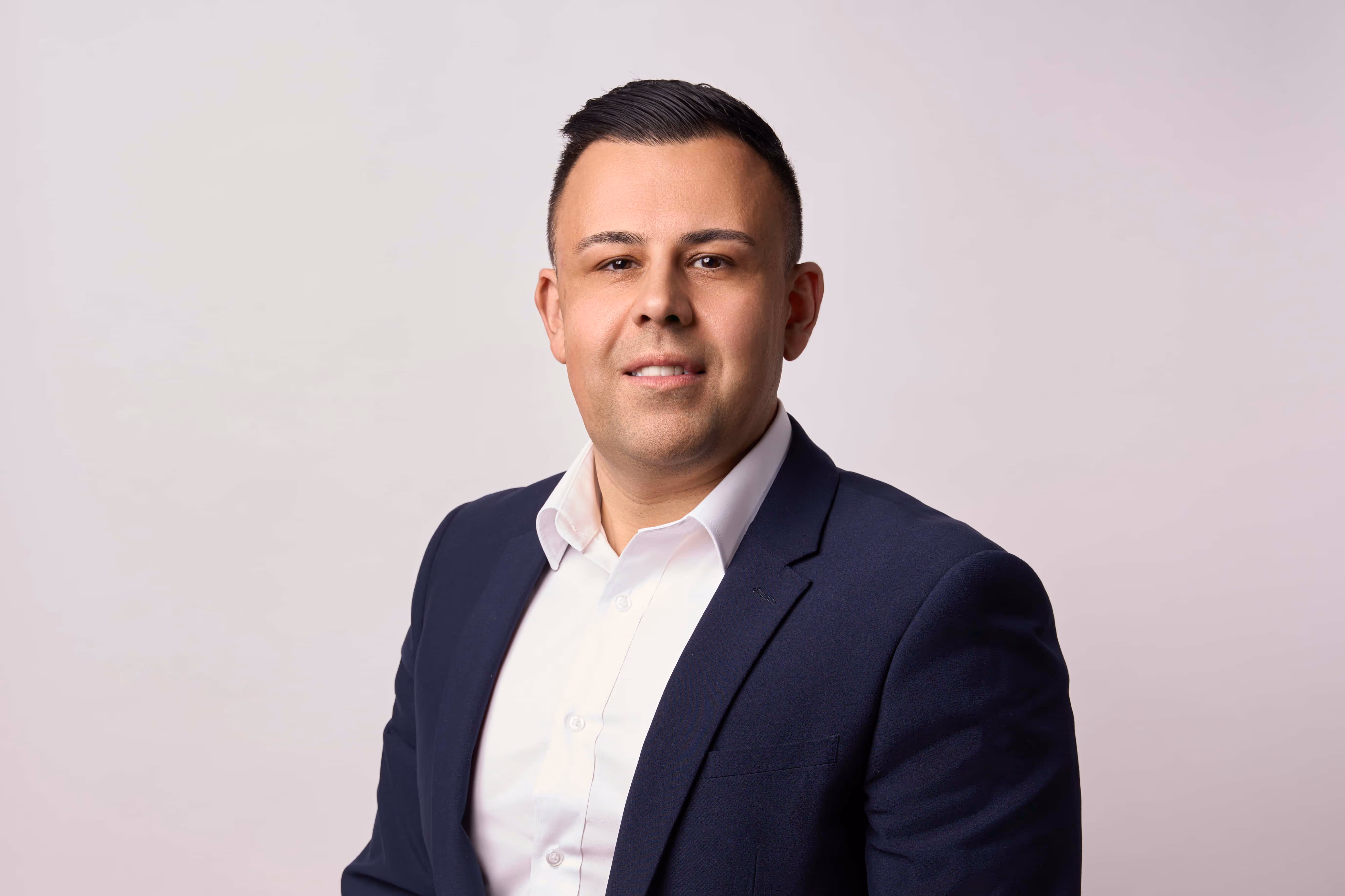 Portrait of a man wearing a navy blazer and white shirt against a light background.