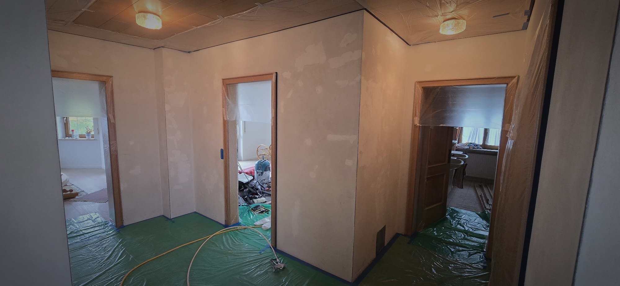 Interior of a house under renovation with plastic sheets covering the floor and door frames leading to different rooms.