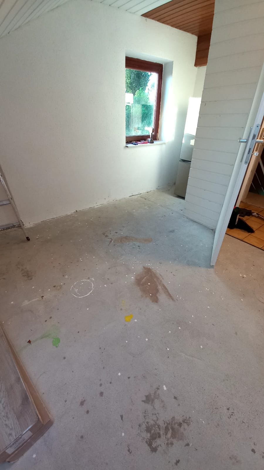Empty room with stained concrete floor, white walls, a window, an open door leading to another room, and a stepladder leaning against a wall.