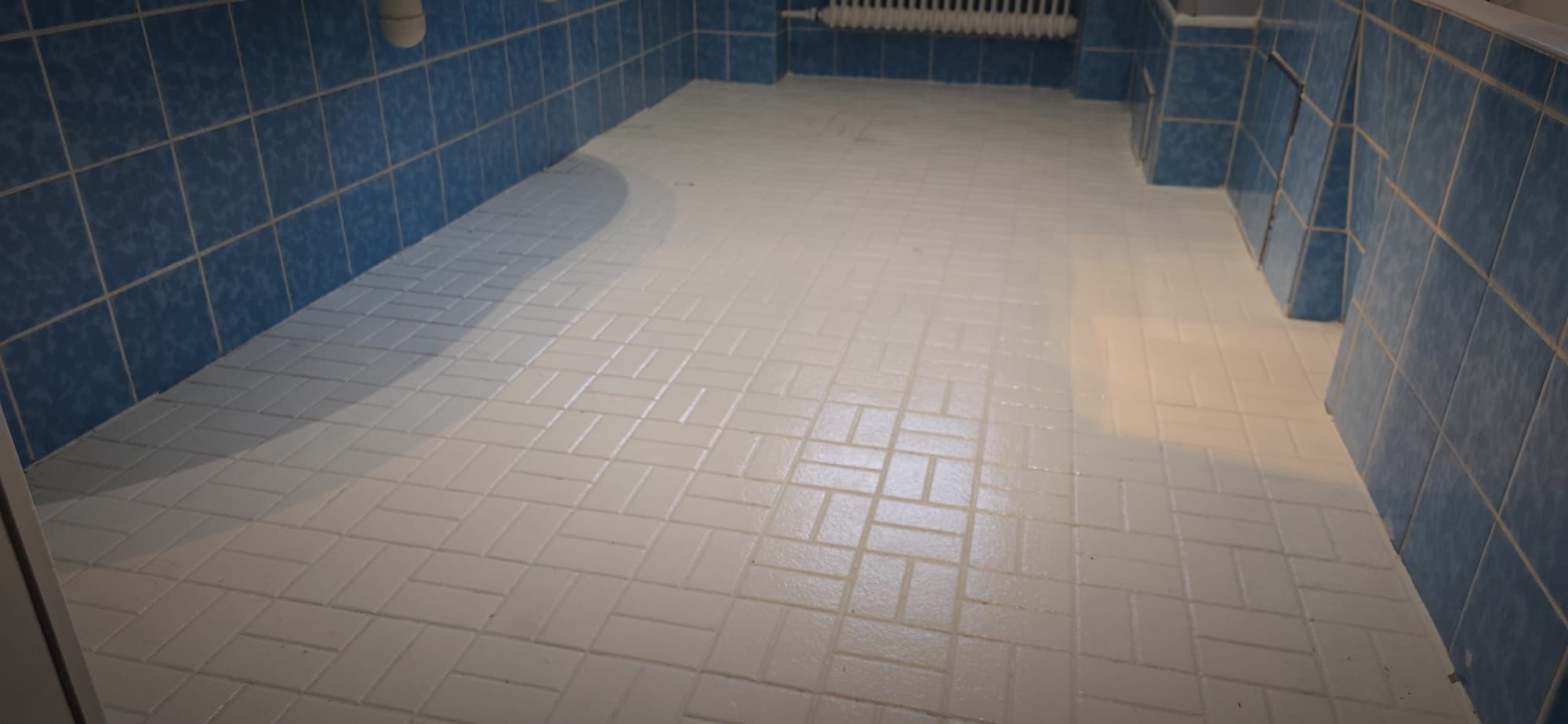 Room with blue tiled walls and white textured tile floor reflecting light.