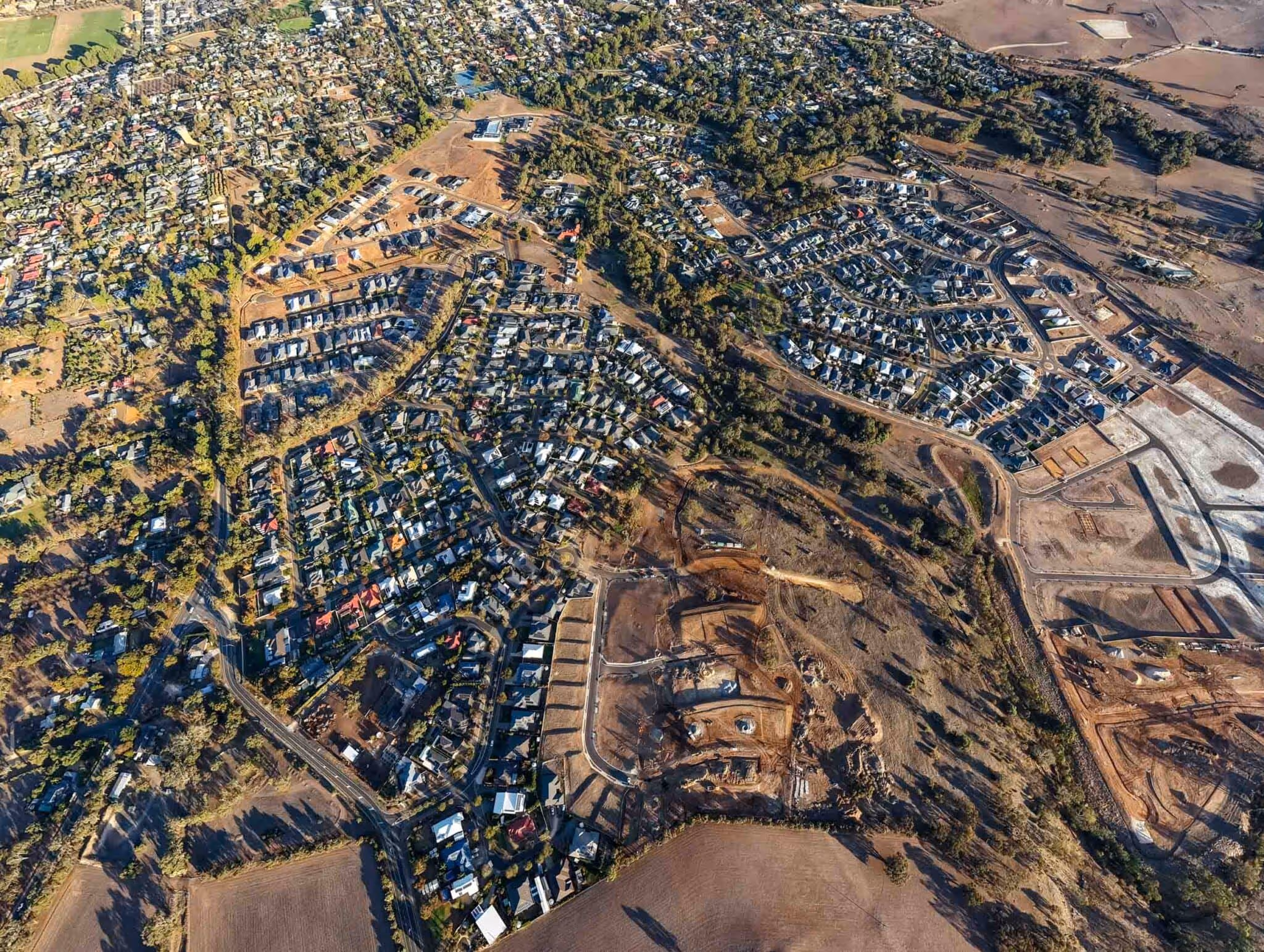 Aerial view of a growing suburban area showing established homes, new housing lots, and surrounding farmland.