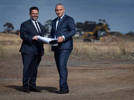 Two men in suits on a construction site holding paper plans.