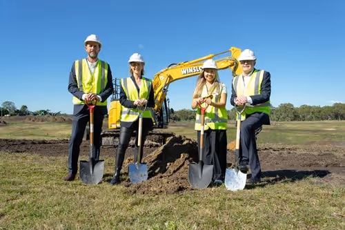 People in corporate wear with hard hats and shovels.