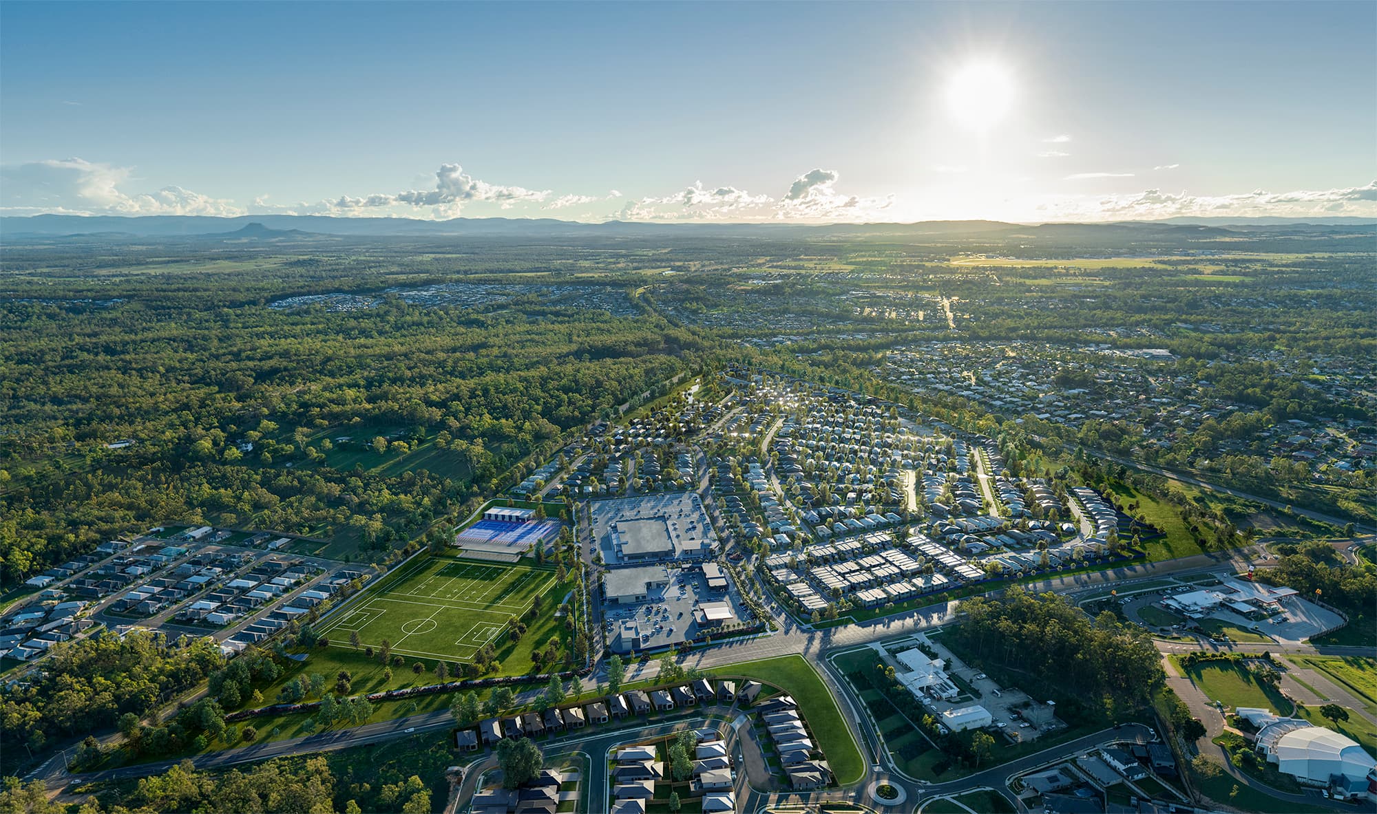 A wide aerial view of a suburban development surrounded by greenery under bright sunlight.
