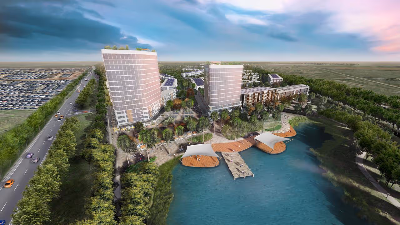 Aerial view of two modern towers beside a lake with boardwalks, greenery and surrounding residential areas.