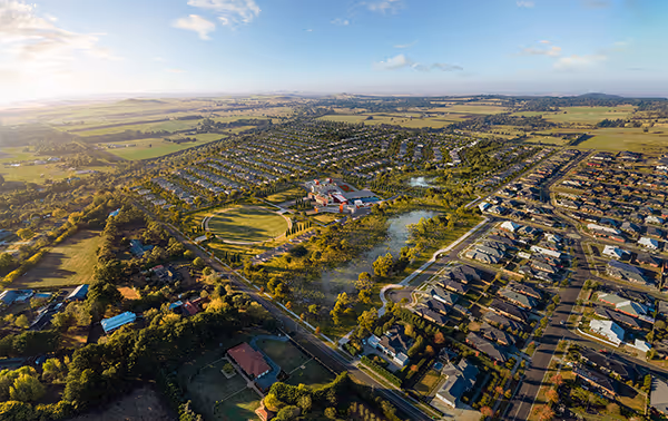 Aerial view of a masterplanned community with homes, parkland and a central lake surrounded by farmland.