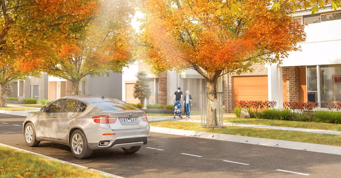 Tree-lined suburban street with autumn leaves as a couple walks a stroller past modern homes and a parked car.