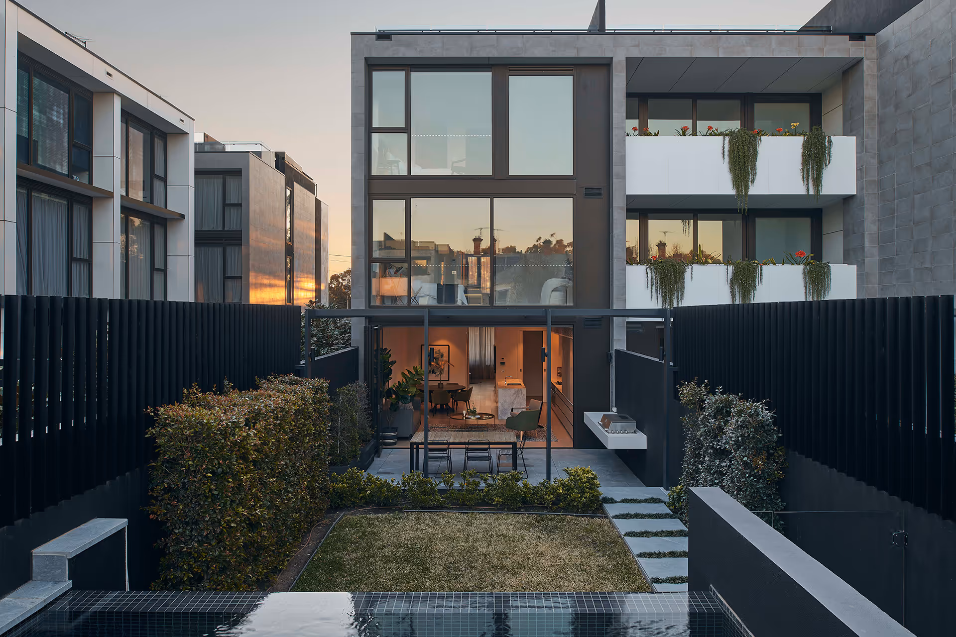 Rear view of modern townhouses facing a private garden and pool area at sunset.