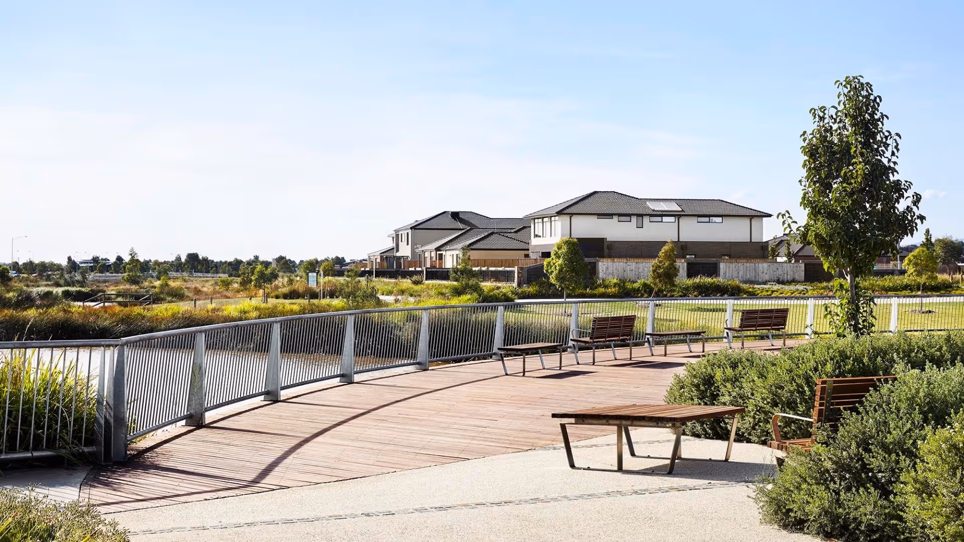 Boardwalk overlooking landscaped wetlands with nearby modern homes and seating areas.