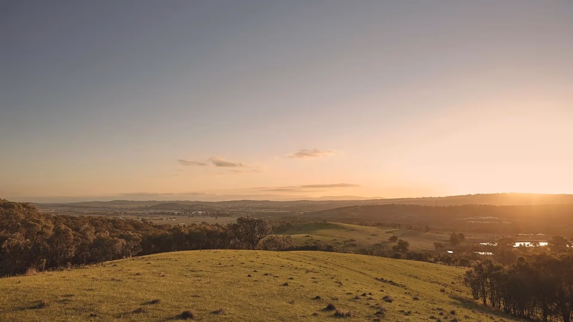 Rolling green hills at sunset overlooking a wide valley and distant mountains.