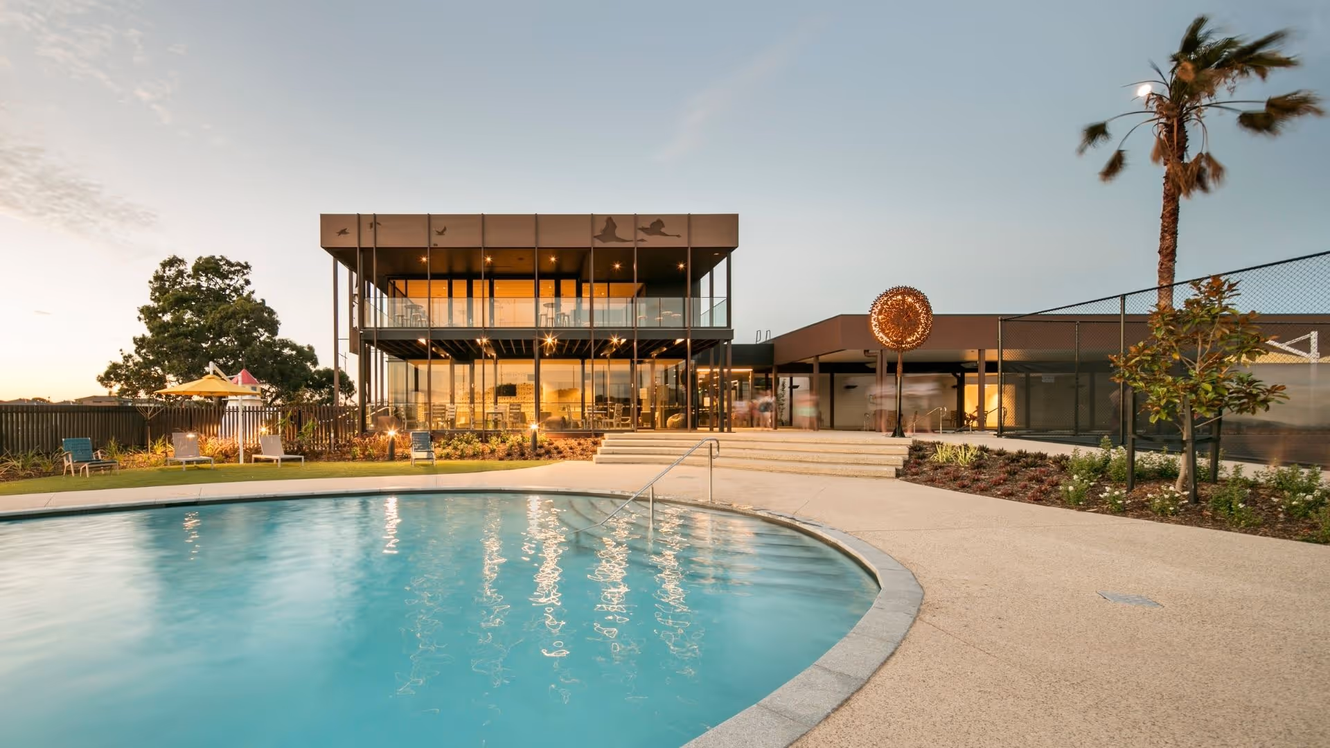 Modern clubhouse at sunset with a resort-style outdoor pool and landscaped surrounds.