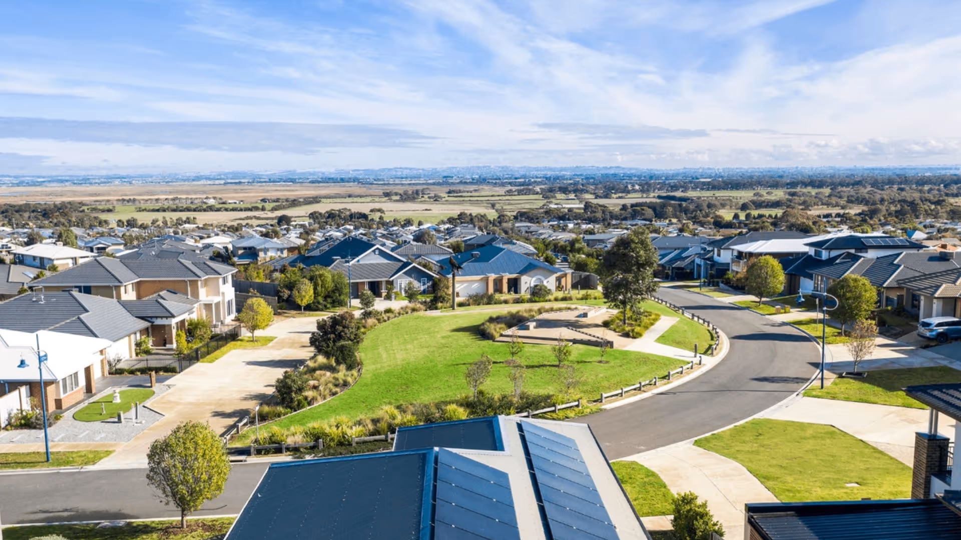 Aerial view of a residential neighbourhood with curved streets and a central green park surrounded by modern houses.