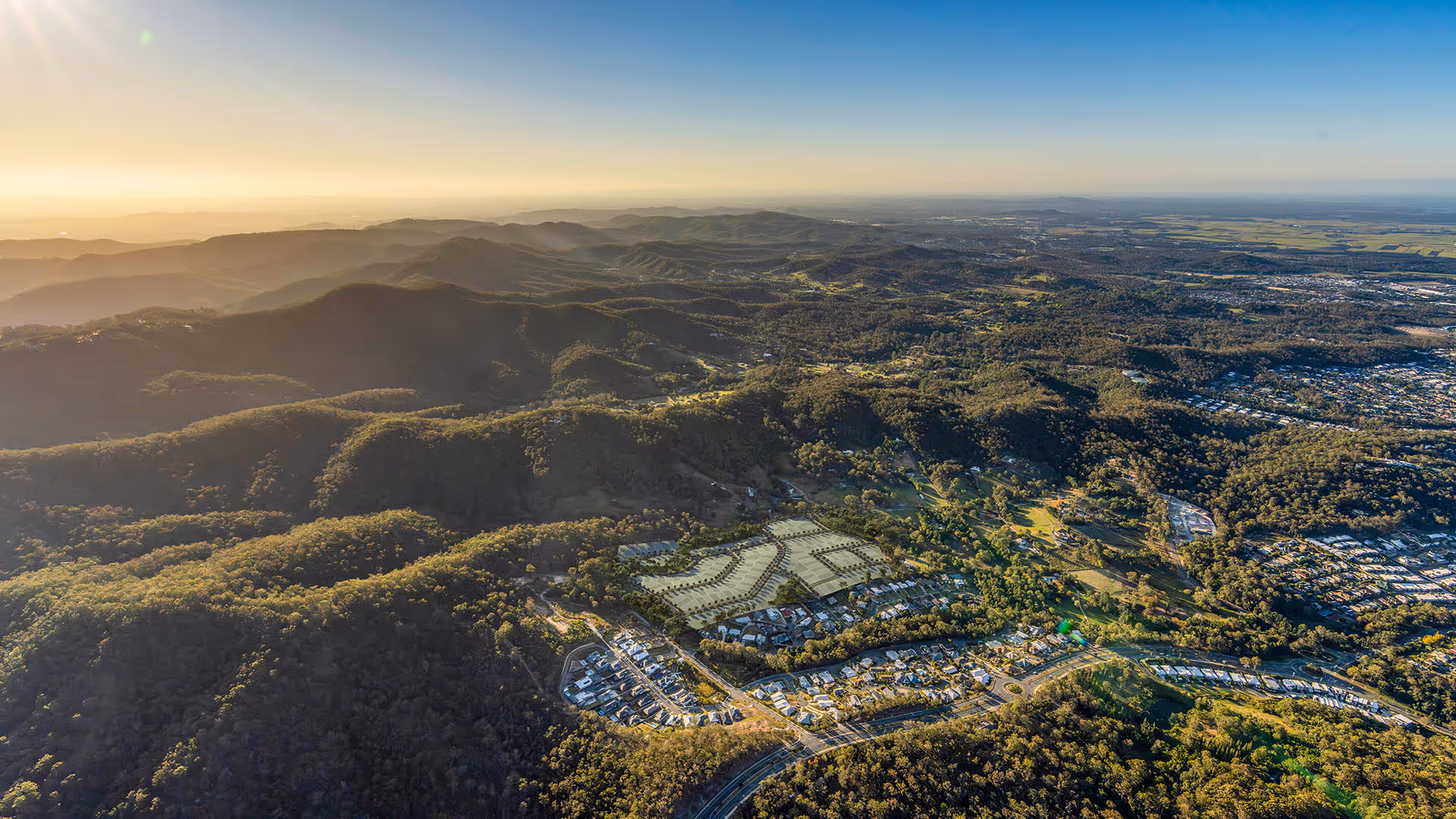 Aerial view of rolling green mountain ranges at sunrise, with a residential development nestled in the valley below.