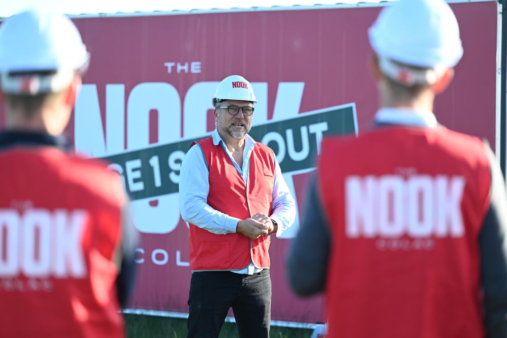 A man in a red Nook vest and white hard hat addresses attendees at The Nook Colac construction commencement, standing in front of branded 'Stage 1 Sold Out' hoarding.