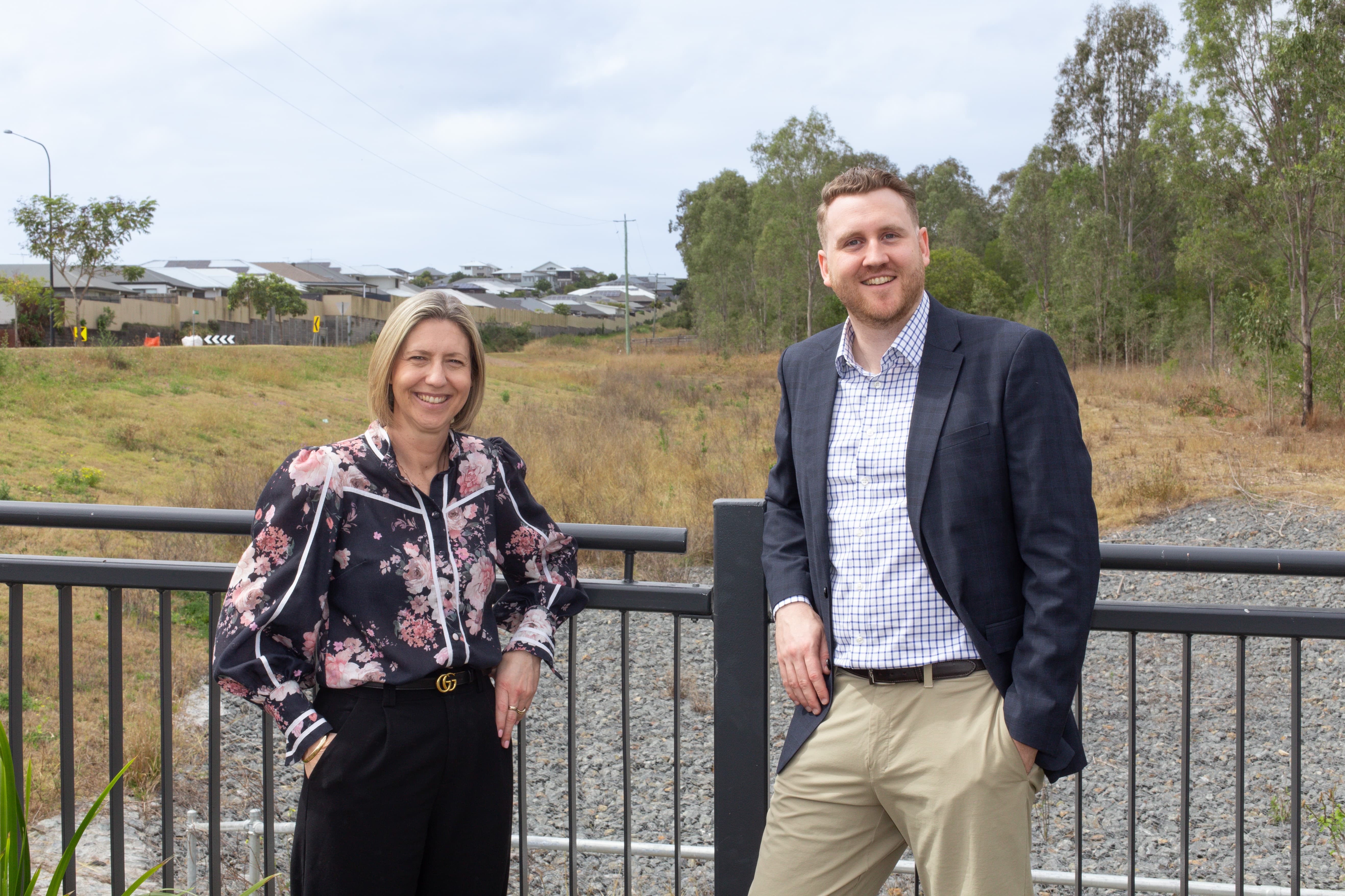 Two people standing in front of railing at the future Silva South Ripley site, with neighbouring homes and bushland visible in the background.