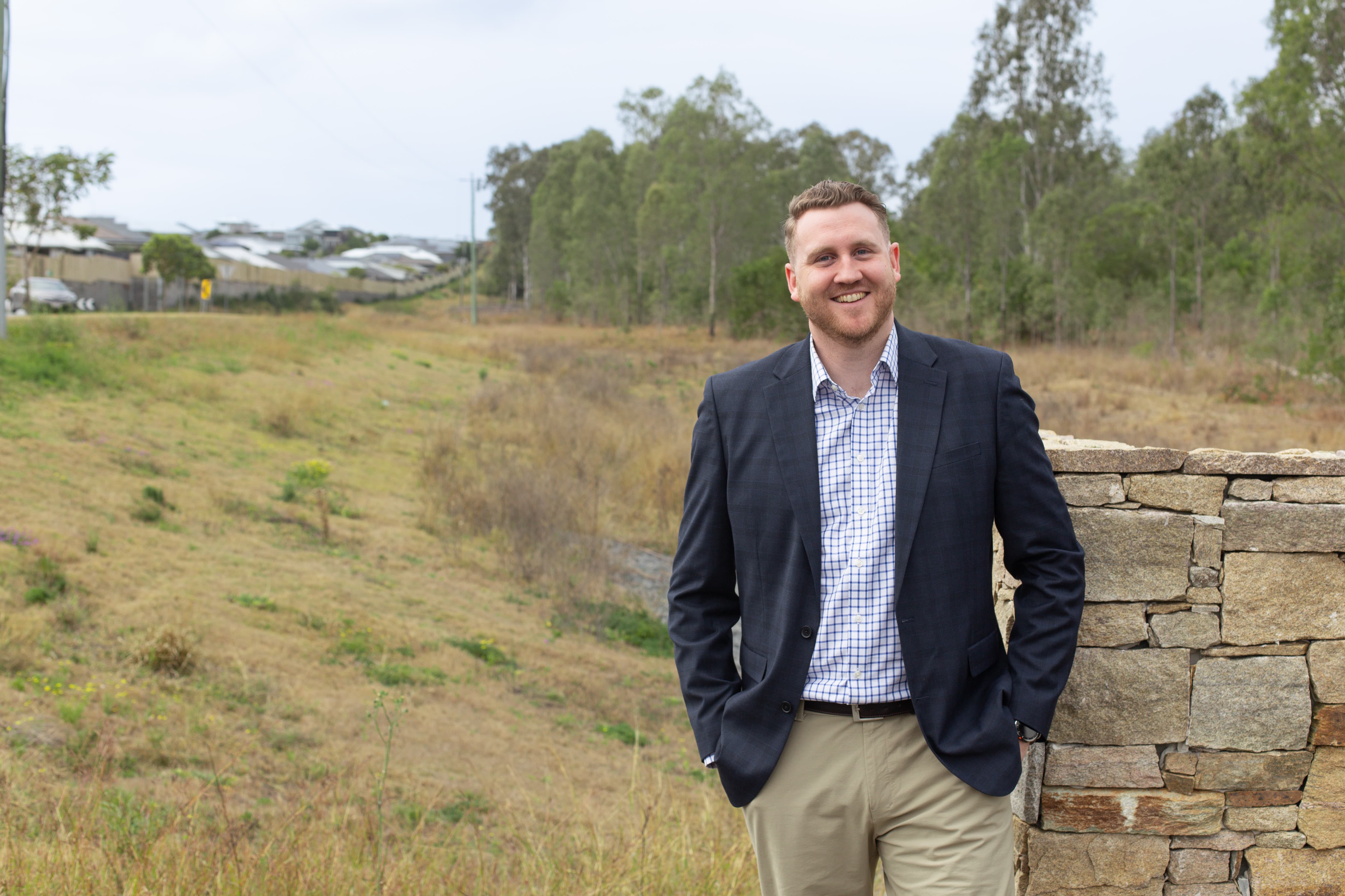 Person standing at the Silva South Ripley site, with open land, established housing and native vegetation visible behind.