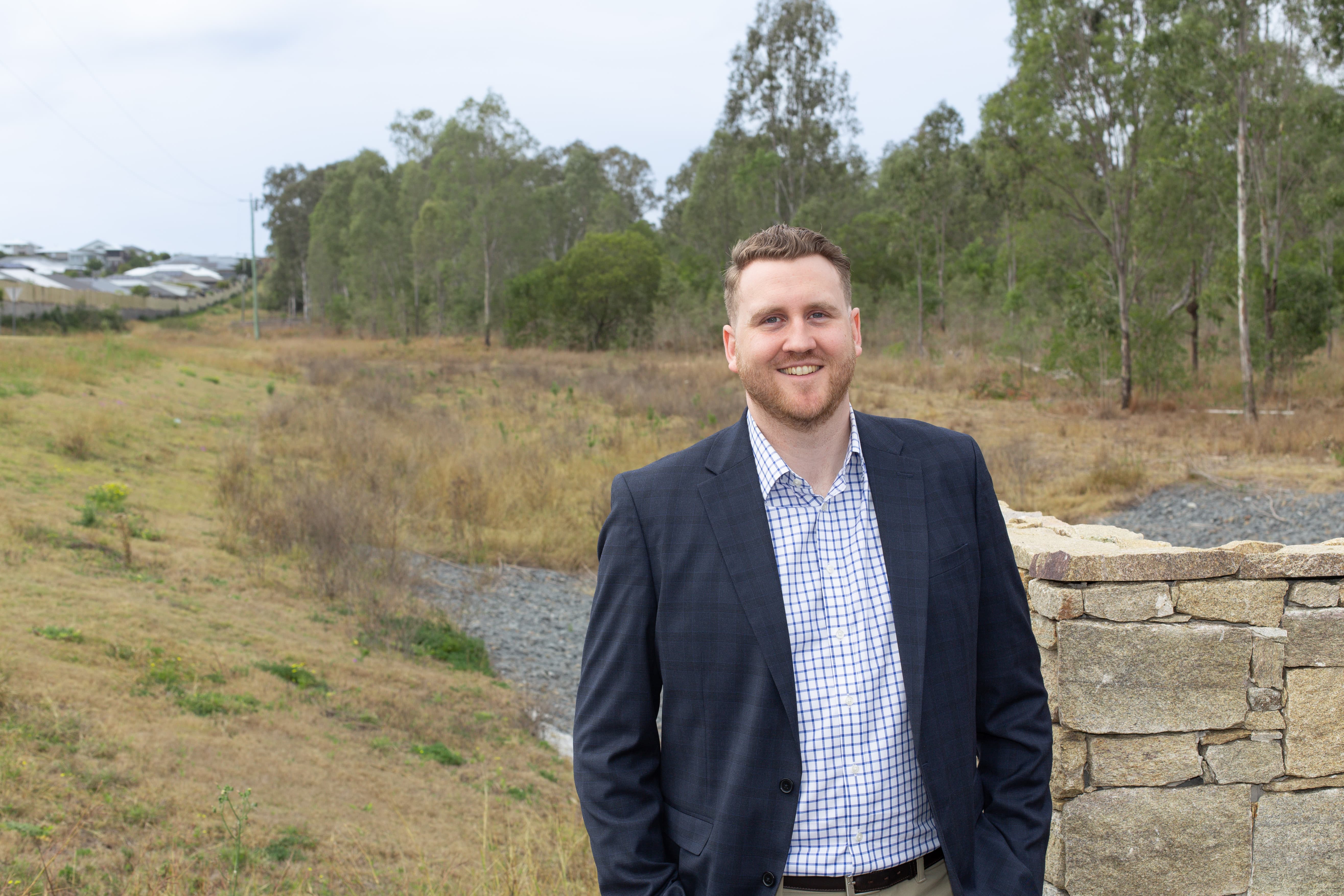 Person standing at the Silva South Ripley site, with open land, established housing and native vegetation visible behind.