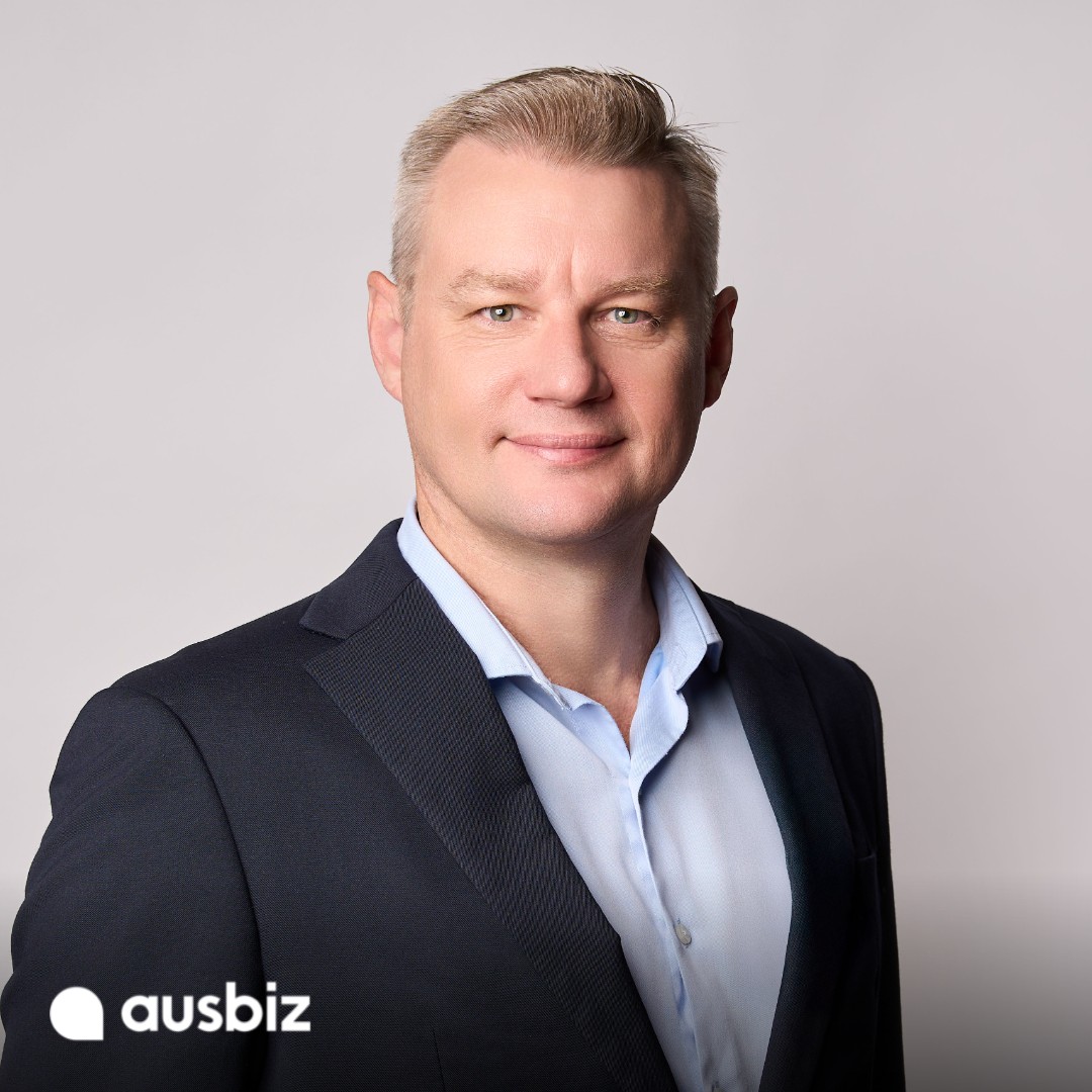 Oliver Hume Chief Economist Matt Bell in a navy blazer and light blue shirt against a light grey background, with the ausbiz logo
