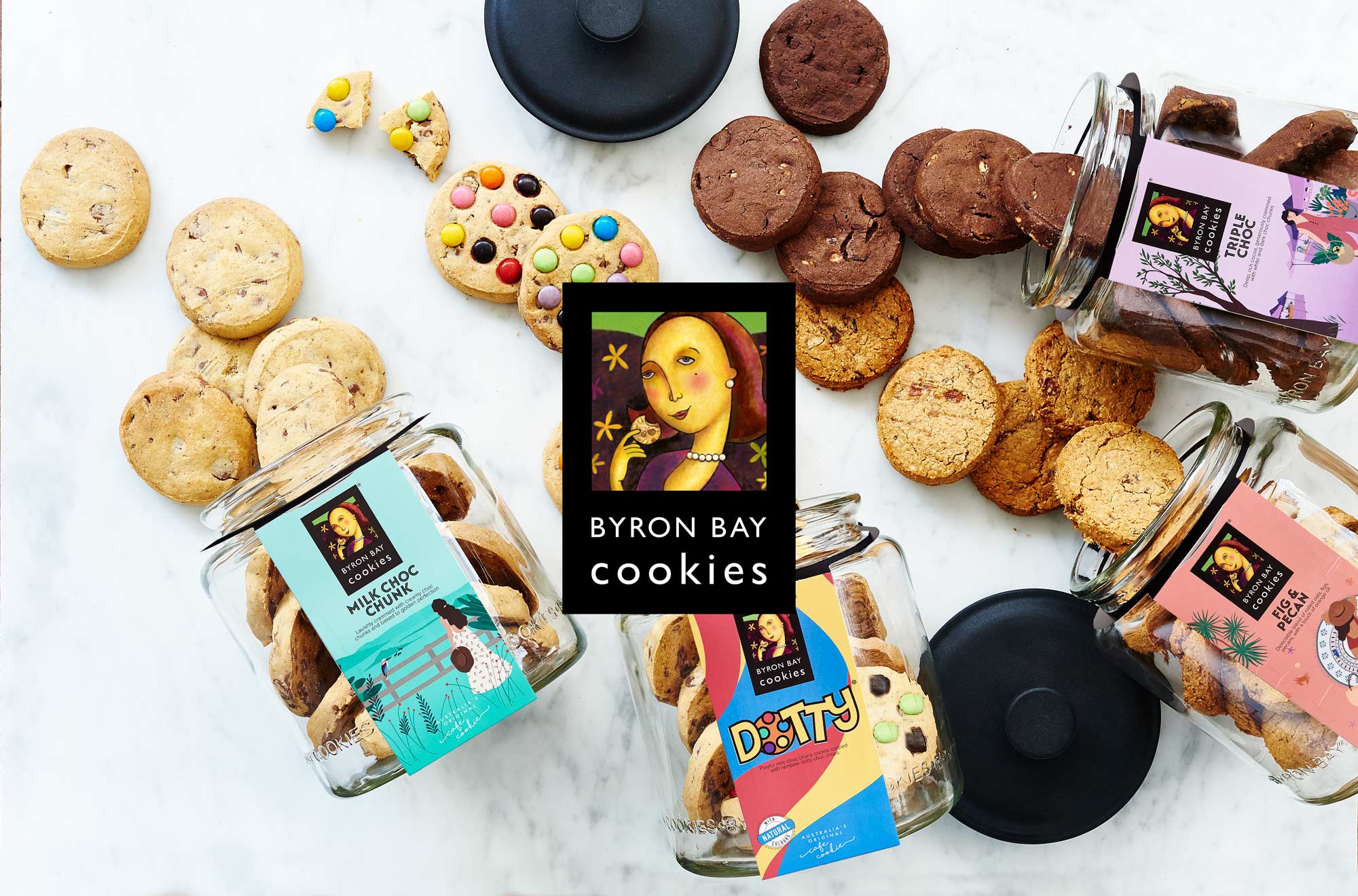 a flat lay of various cookies spilling out of jars on a white stone bench. Byron Bay Cookies logo is in the foreground.