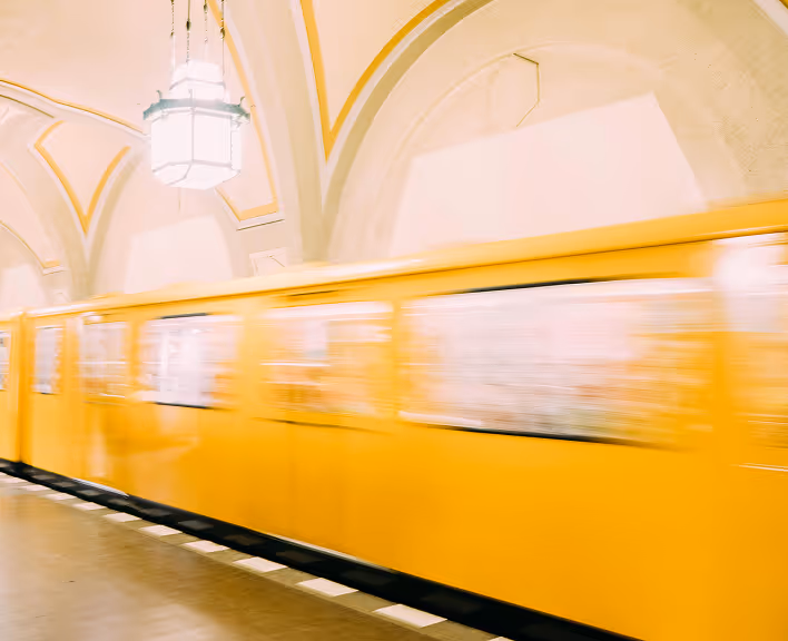 Yellow subway train moving through an arched, well-lit underground station.