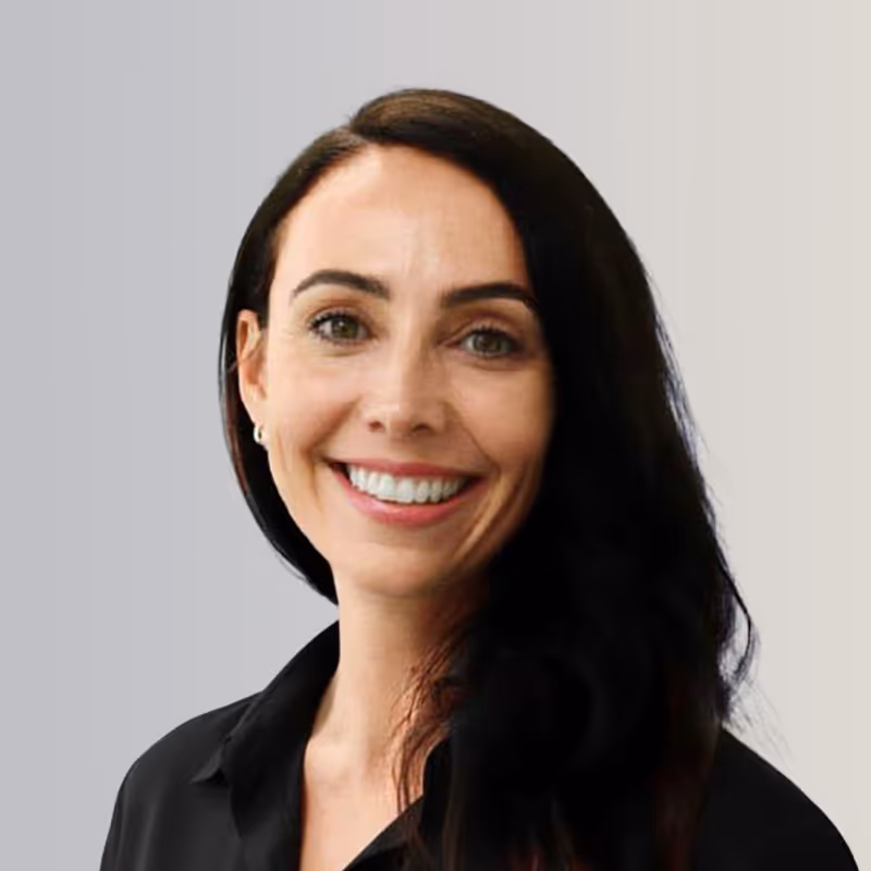 Smiling woman with long dark hair wearing a black shirt against a gradient gray background.