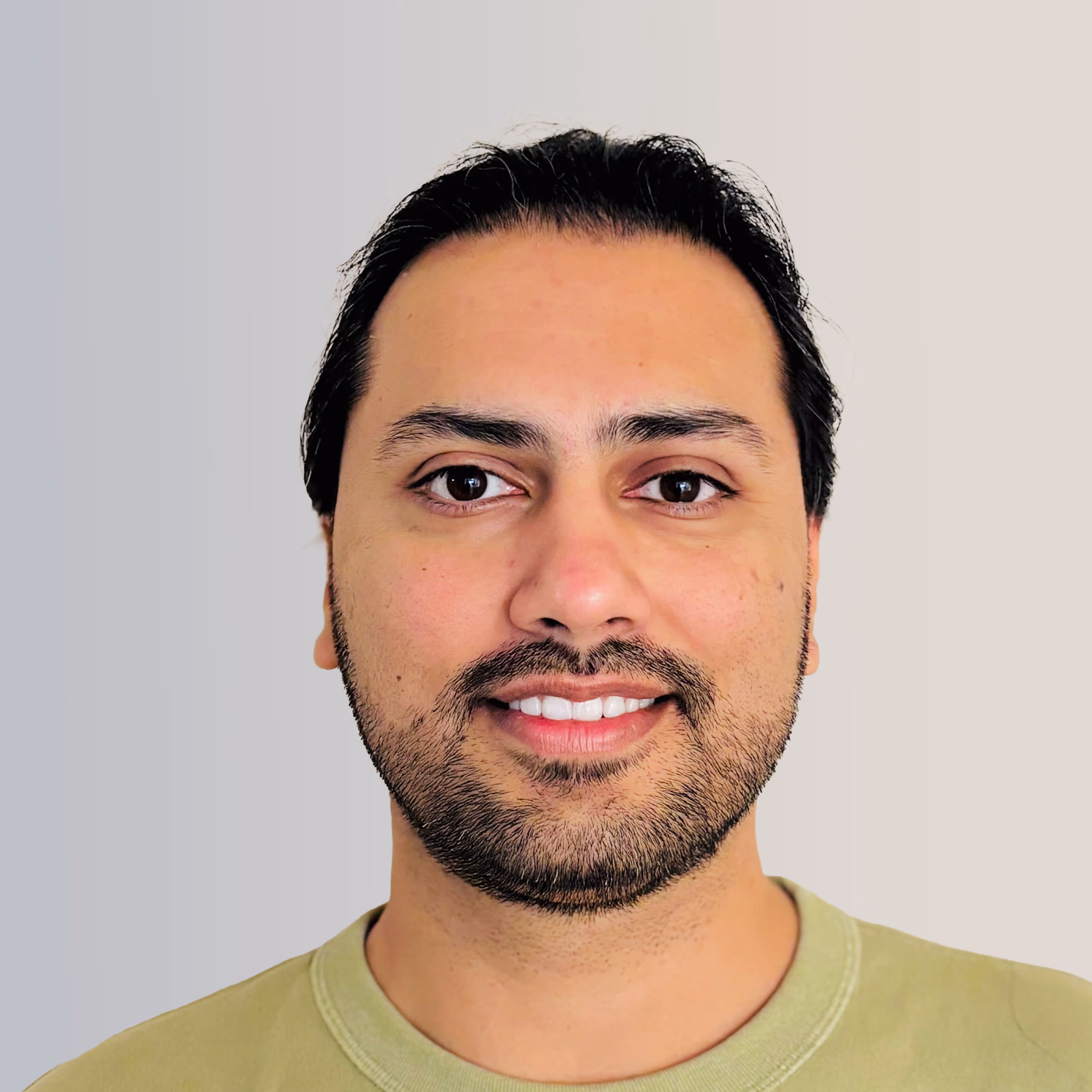 Smiling man with short black hair and beard wearing a light green shirt against a gray gradient background.