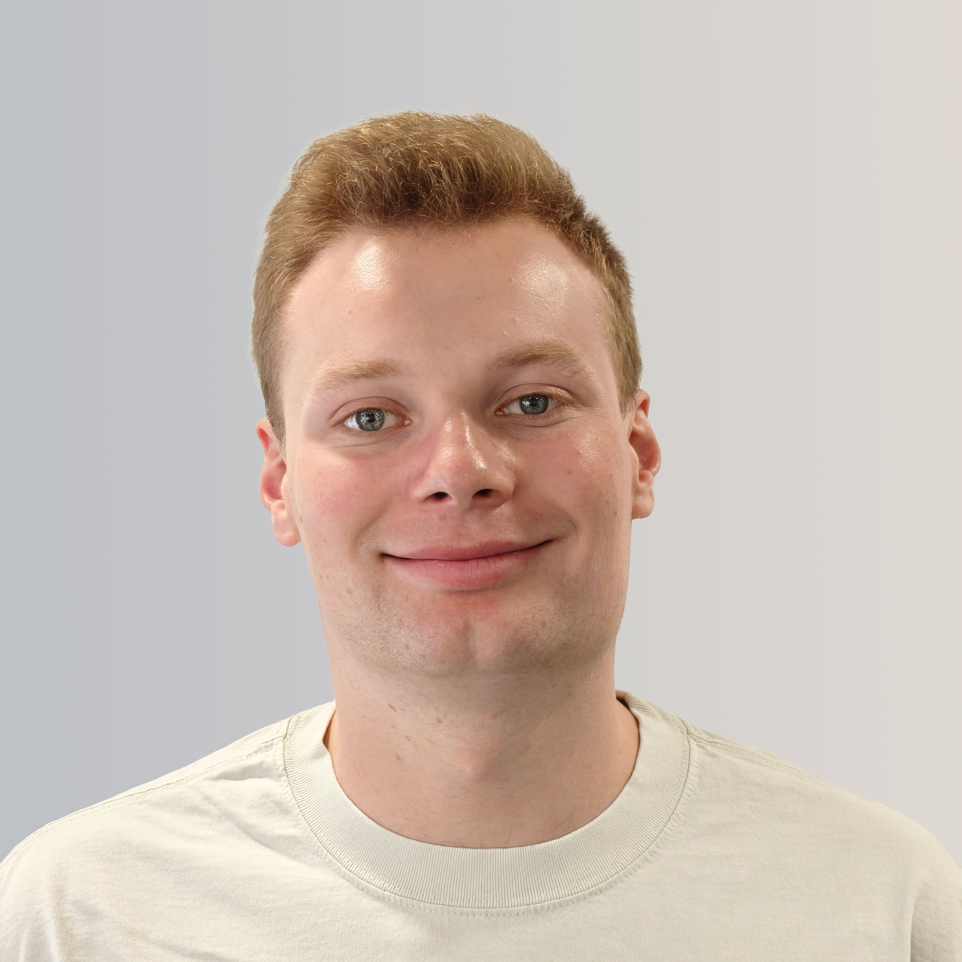 Smiling young man with short light brown hair wearing a white crew-neck t-shirt against a light gradient background.